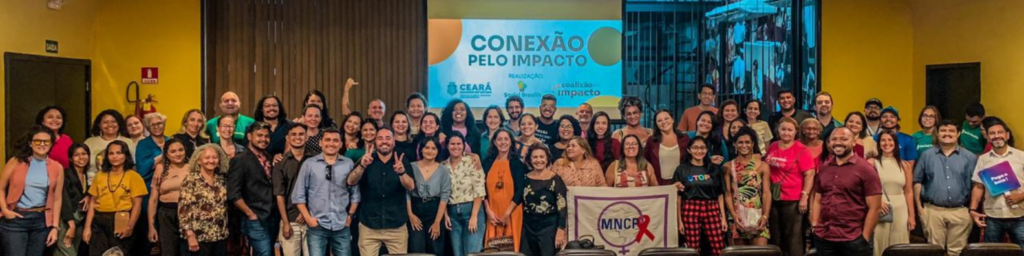 Empreendedores sociais reunidos em Fortaleza para foto diante de um telão no evento Conexão pelo Impacto, promovido por Corredores Digitais e Social Brasilis