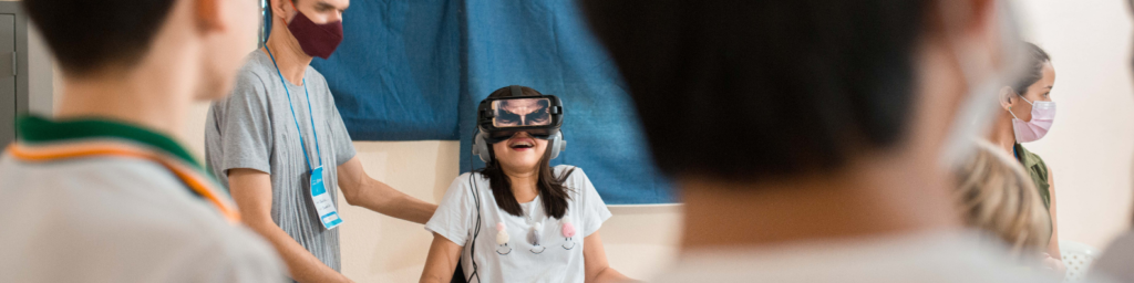 Uma menina sorrindo e com oculos de realidade virtual, cercada por um grupo, ilustrando a educação 4.0 e a transformação do ensino nas escolas.