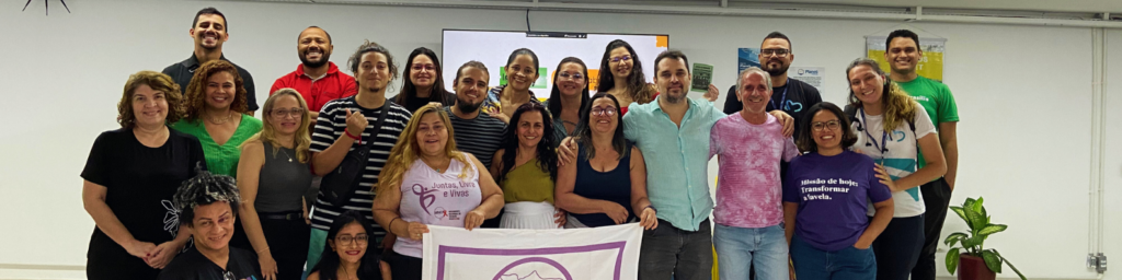 Grupo de pessoas sorrindo para a câmera em frente a um grande telão no Incubação Social Lab, Fortaleza.