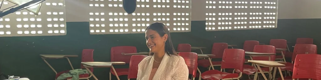 Manu Oliveira, fundadora do Social Brasilis, sentada em sala de aula com cadeiras vermelhas, preparando-se para o Prêmio RioMar Mulher 2025.