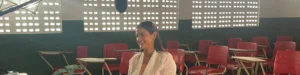 Manu Oliveira, fundadora do Social Brasilis, sentada em sala de aula com cadeiras vermelhas, preparando-se para o Prêmio RioMar Mulher 2025.